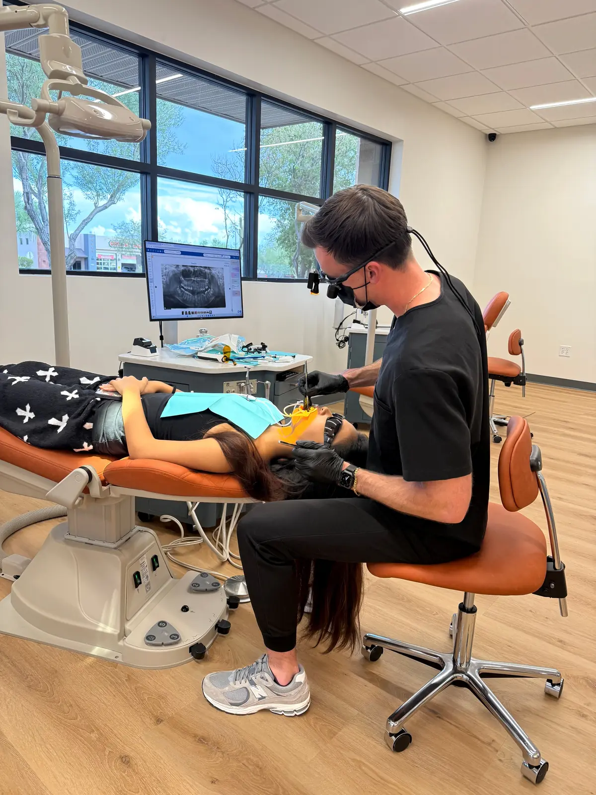 Dr. Romans working chairside on a patient at Romans Orthodontics, with a panoramic x-ray on the monitor