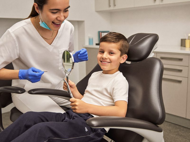 A young child looking at their teeth in a hand mirror at a first orthodontic visit